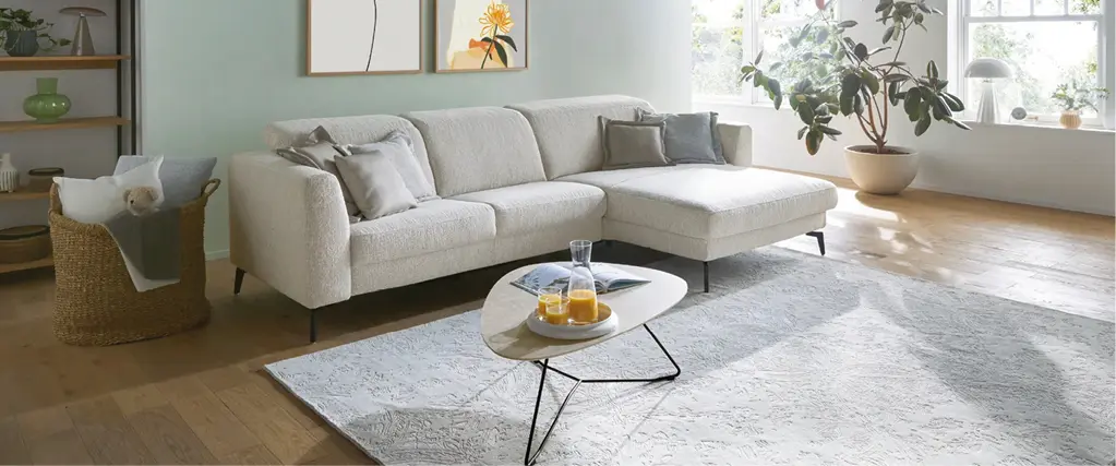 Helles Wohnzimmer mit modernem Ecksofa, Dekokissen und Couchtisch. Zeitlose Wohnmöbel schaffen eine gemütliche Atmosphäre und zeigen zeitgemäßes Wohndesign für stilvolles Einrichten.